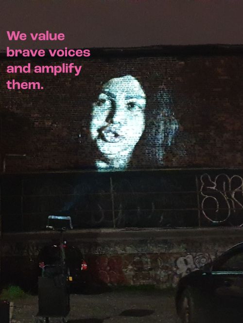 A picture of a woman talking is being projected against a brick wall at night.