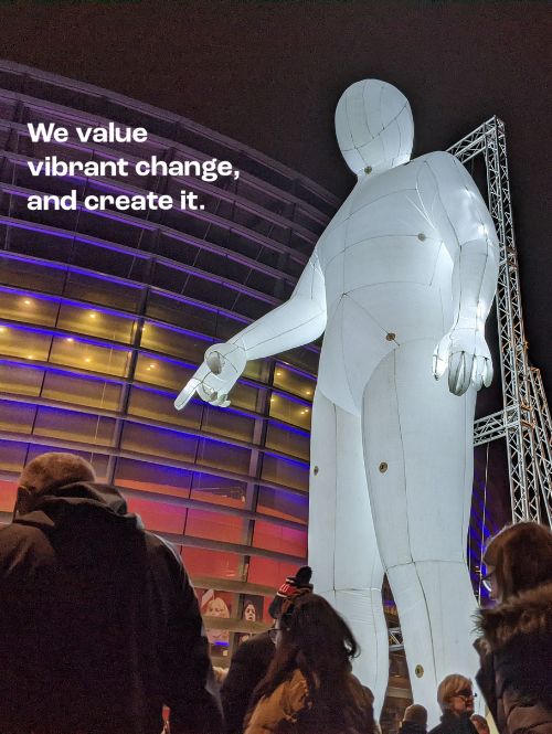 A giant illuminated figure is pointing to the ground at an outdoor event.