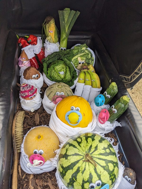 A pram with vegetables and fruits, dressed as babies.