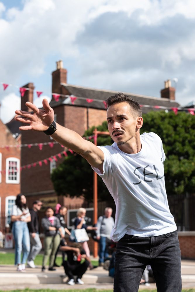 A Dancer reaches his outstretched arm to an audience member at an outdoor performance.