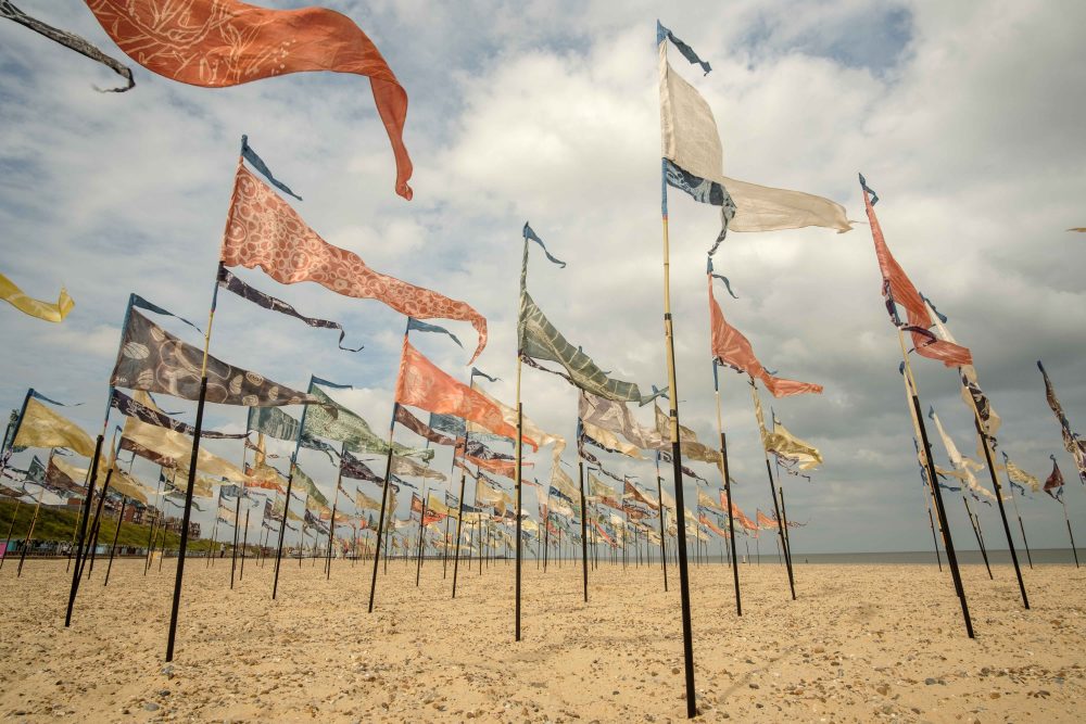 A series of painted silk pennants are decorating a beach and blowing in the wind.