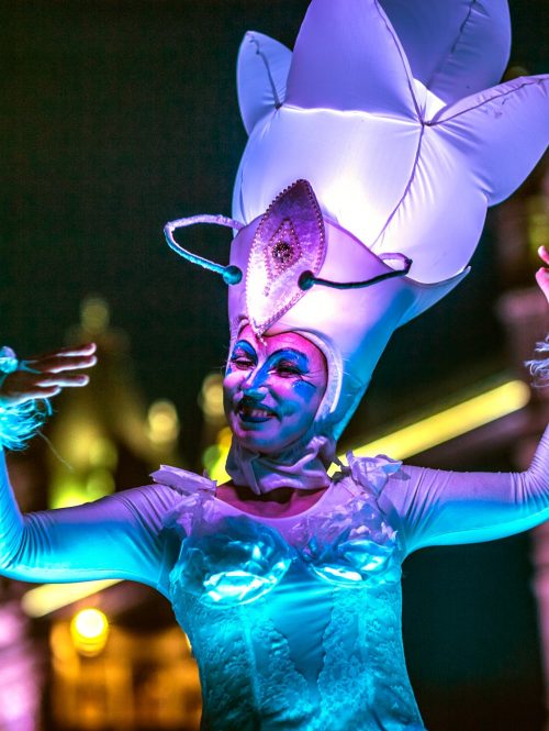 A woman in a blue and pink lit costume with a big enlightened headpiece.