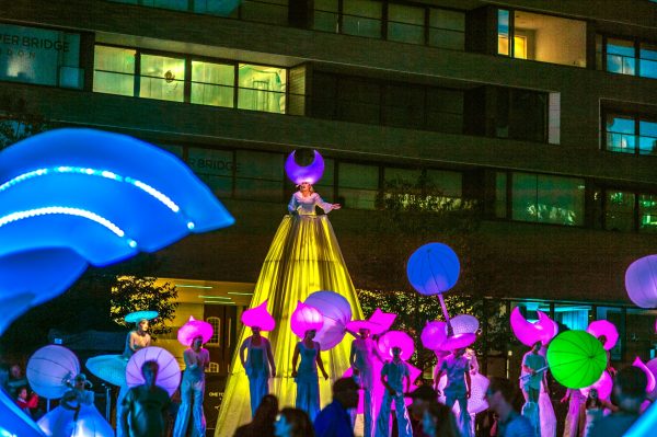 A group of illuminated street performers parade on stilts through the streets of London.