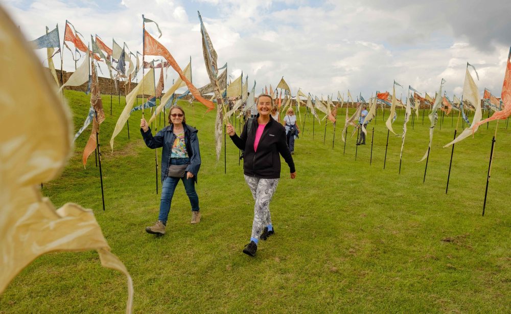 A series of painted silk pennants are decorating an open hillside. A group of people are also holding pennants in the air.