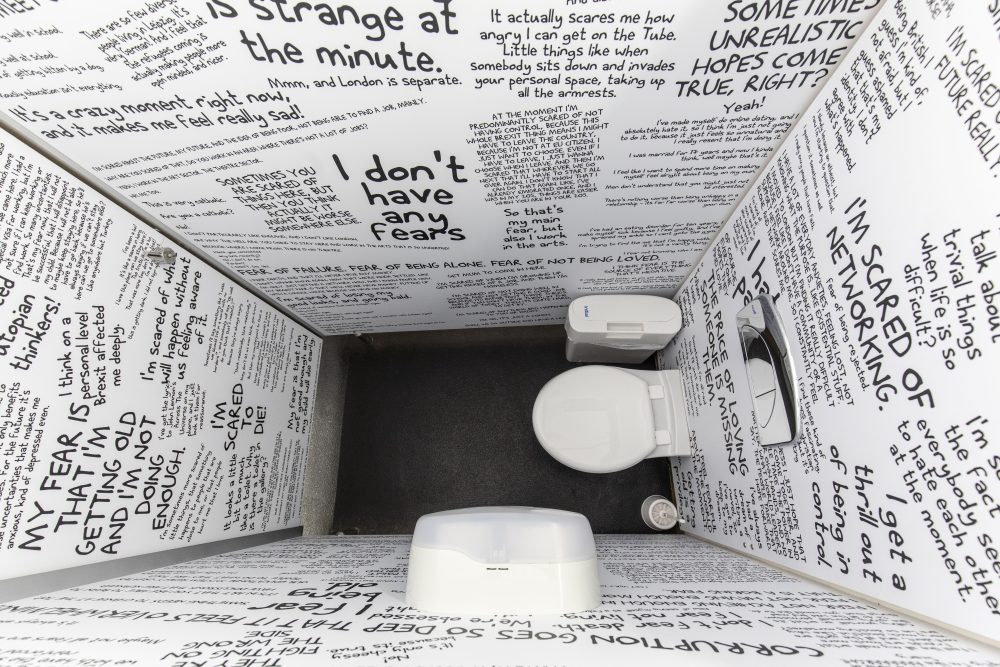Birds-eye view of a toilet cubicle, with its white walls full of text written in black.
