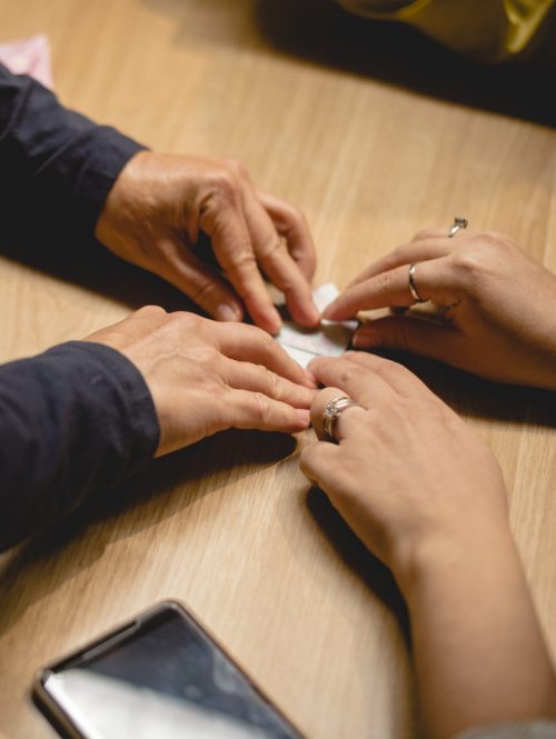 Two pair of hands on a table, folding a piece of paper together.