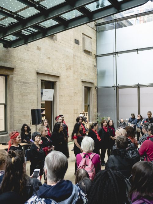 Audiences standing in an indoor space, looking at performers.