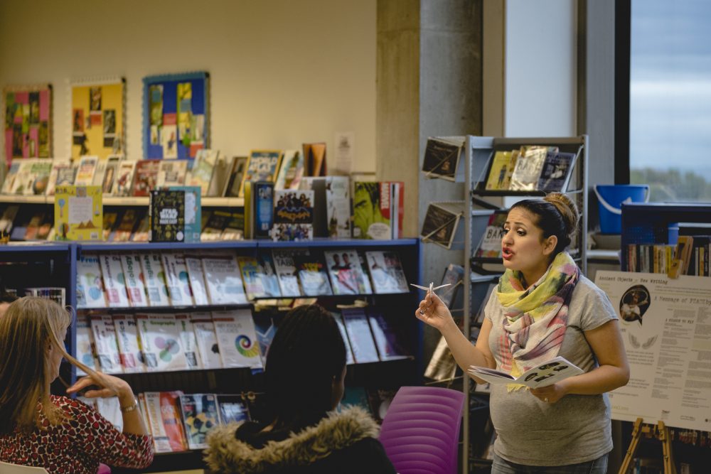 A pregnant woman is talking to some people in a library.