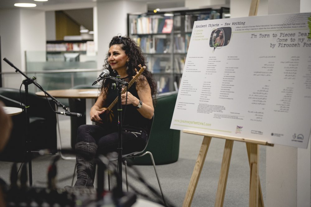 An artist is playing the violin in a library, in the foreground is an information stand.