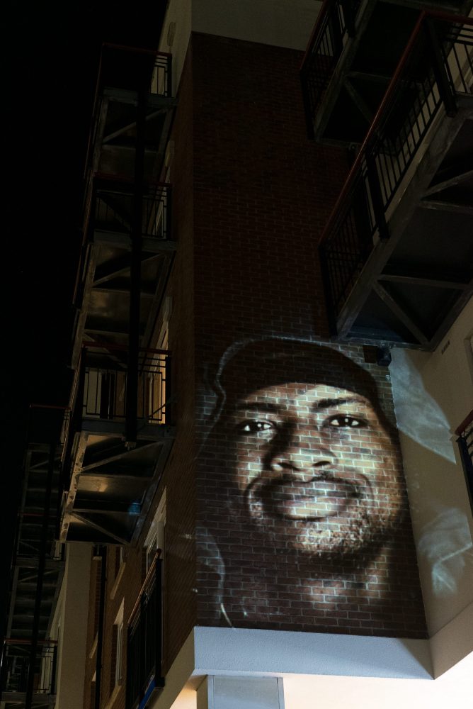 This image shows a portrait of a man that is being projected against a wall in a dis-used part of Portsmouth town centre.
