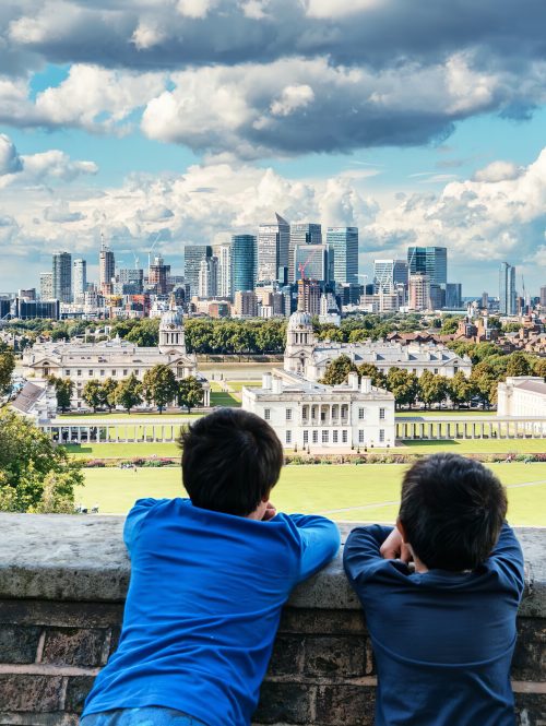 Two young children lean against a wall overlooking the Old Royal Naval College in Greenwich.