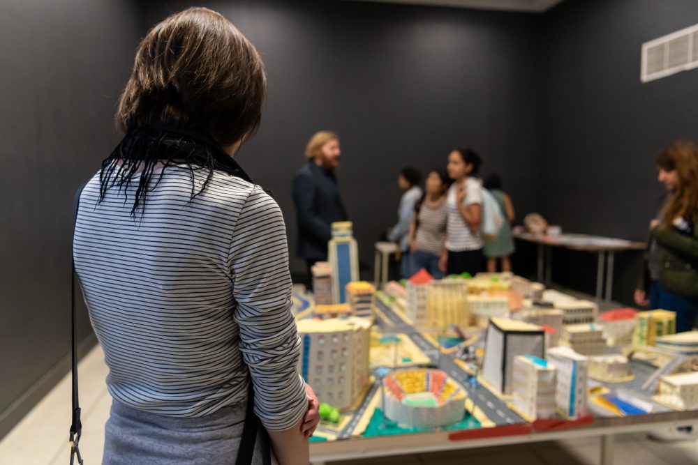 An audience member looking at a model city in an indoor space.