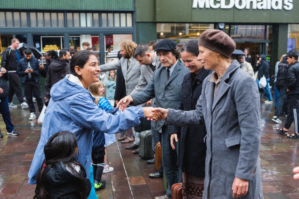 A group of performers shaking hands with audiences members on an outdoor square.