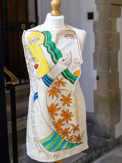 A simple white dress sits on a mannequin, it is decorated with faces.