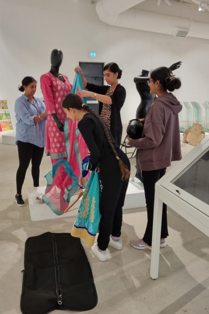 A group of women are dressing a mannequin in a Sari.