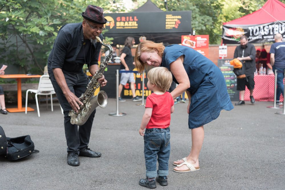 Two people listening to a musician on an outdoor square.