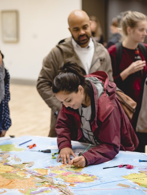 A group of people gather around a map of the world in a creative consultation