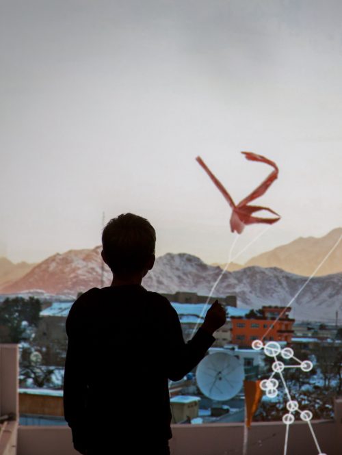 A child standing in front of a projection of a city and kites in the air.