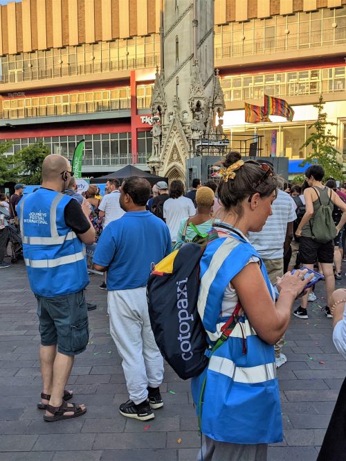 People in blue high-vis vests talking to audience members on an outdoor square.