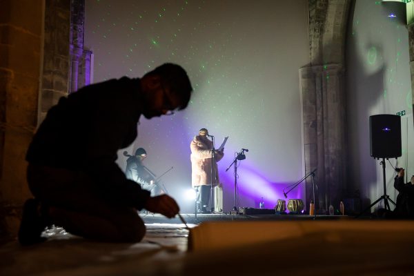 An artist painting on the floor, with a performer at a microphone in the background.