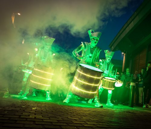 Glowing green drummers in military style costumes please some illuminated drums.