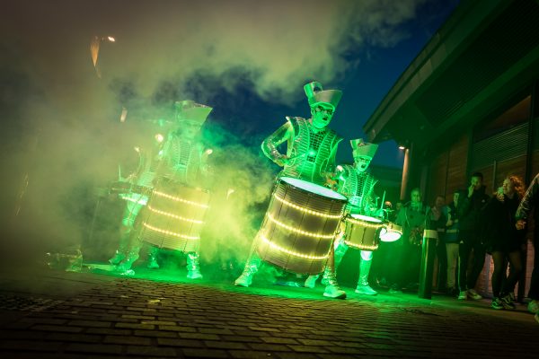 Glowing green drummers in military style costumes please some illuminated drums.