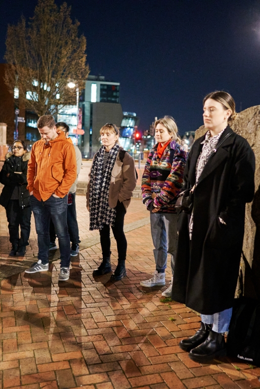 Participants of The Midnight Run stand together on an outdoor square by night with their eyes closed