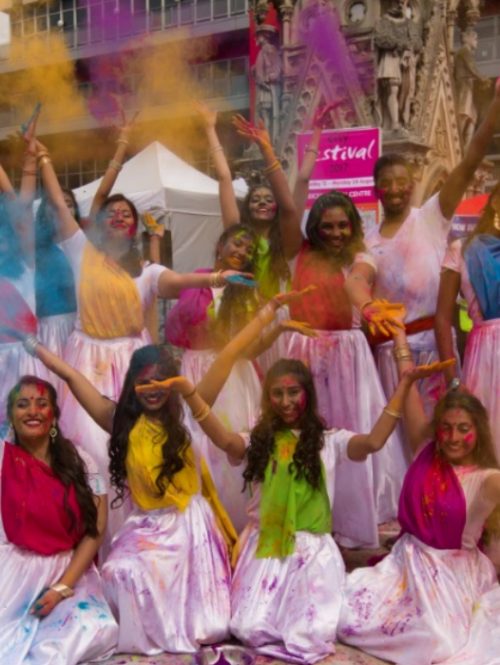 A group of young dancers throwing coloured powder into the air.