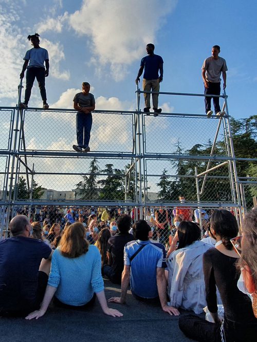 Audiences watching dancers perform on an outdoor metal construction.