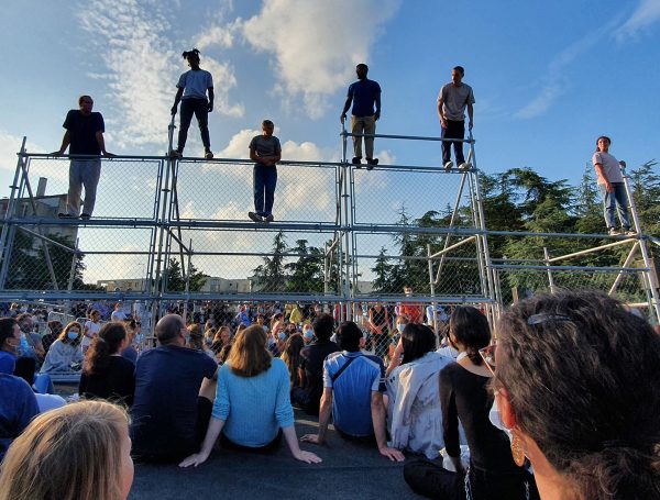 Audiences watching dancers perform on an outdoor metal construction.