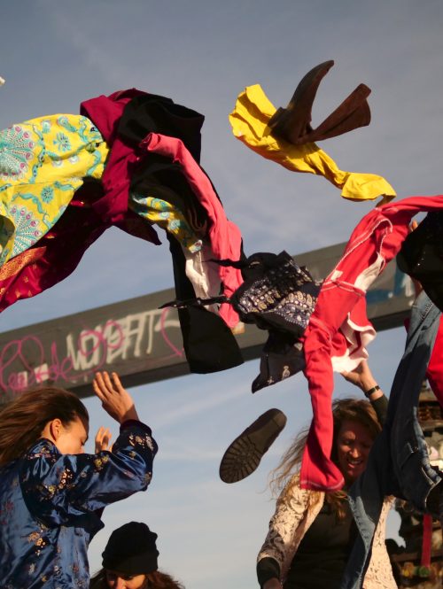 Performers throwing clothes into the air in an outdoor industrial setting.