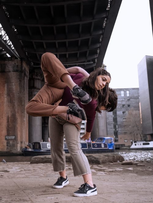 Two performers in a dance position, where one carries the other, in an industrial area.