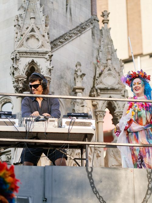 Two people standing on top of a carnival float in front of Leicester's Clock Tower at Journeys Festival International in 2022.