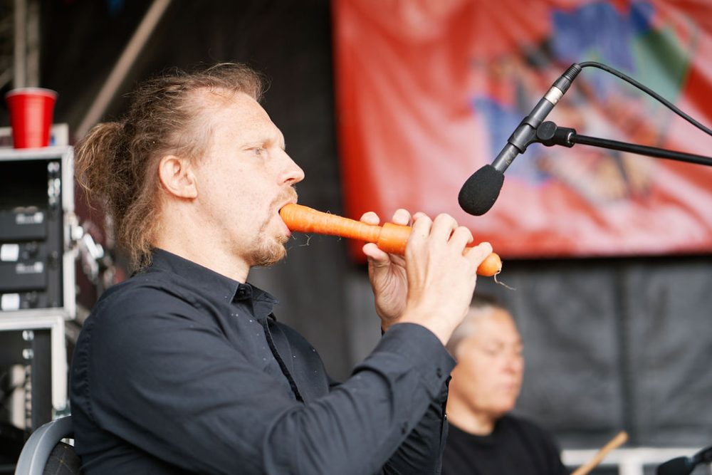 A man in a band plays a carrot like a flute.