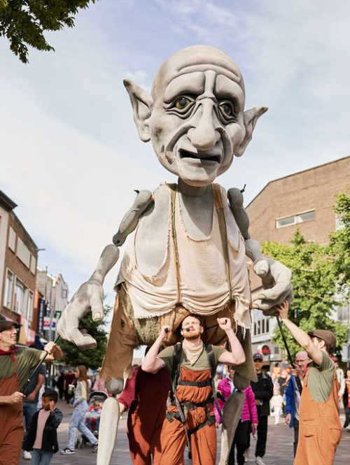 A giant puppet carried and operated by a group of performers on an outdoor square.