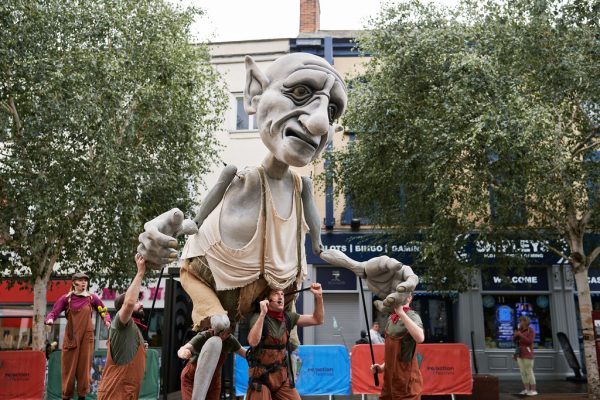 A giant puppet carried and operated by a group of performers on an outdoor square.