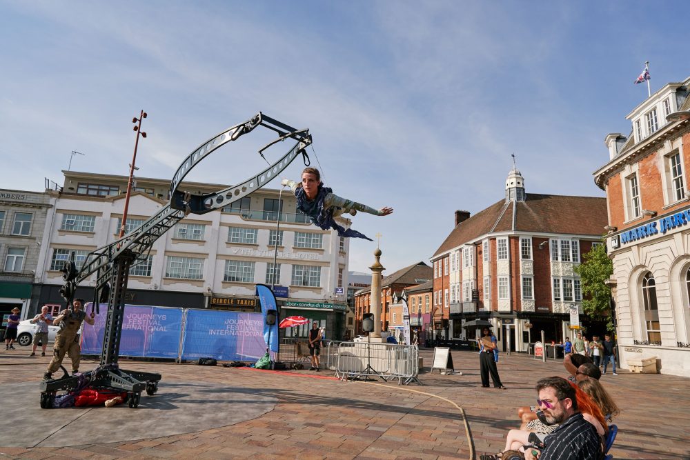 A female performer in the air on a gyroscopic flying machine on an outdoor square.