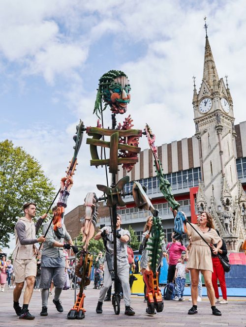 A giant puppet walking alongside audience members at Leicester's Clock Tower.