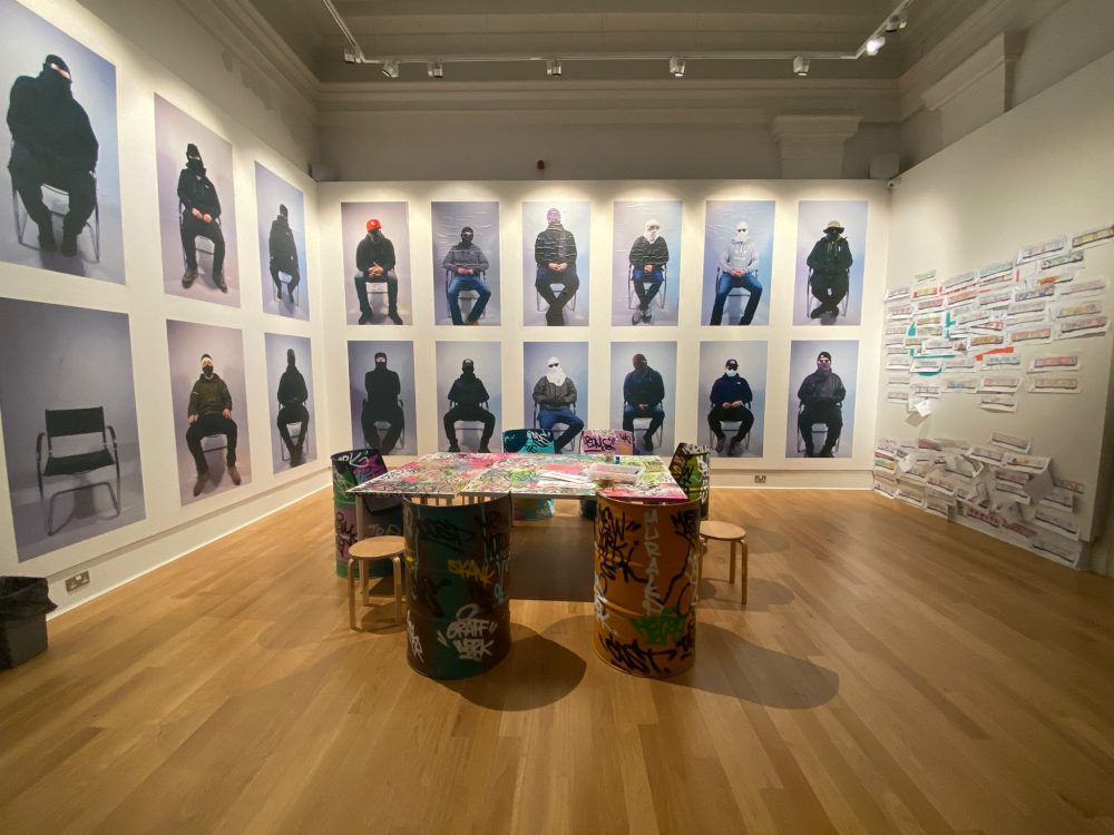 This picture shows a gallery of early days American street artist portraits, all of the people in the portraits are wearing balaclavas to protect their identity.