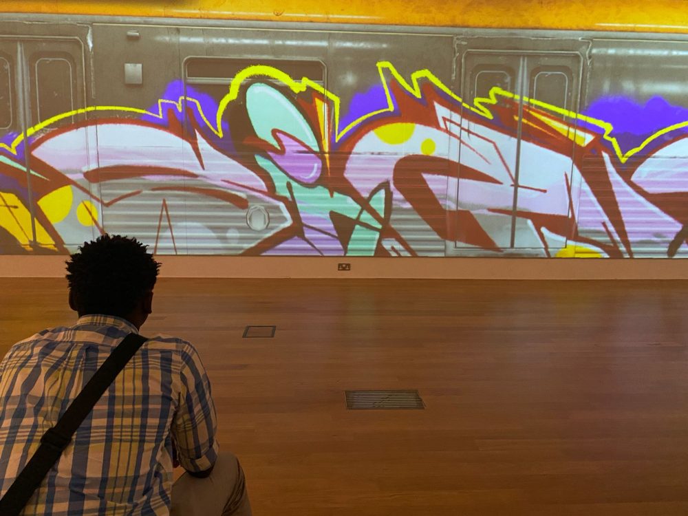 This picture shows a young man sitting in front of an exhibition about Graffiti on trains at Leicester Museum and Art Gallery.