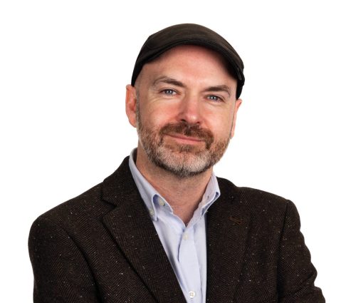 A portrait image of Paul Steele. He wears a flat cap and a dark suit.