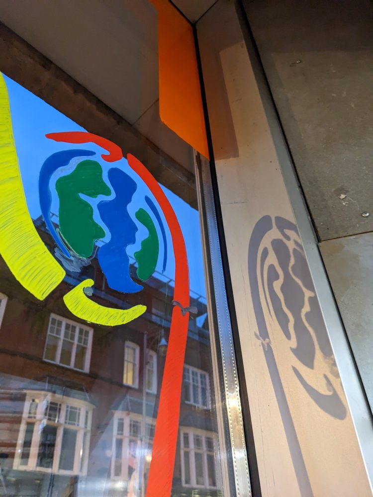 Illustrations of two hands in yellow and red holding our planet drawn onto a window, with it's shadow reflecting on the inside wall.