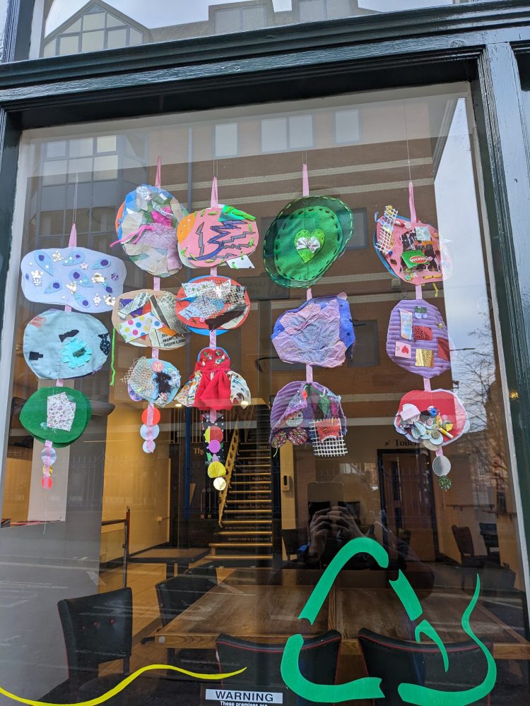Giant sequins displayed hanging in a window at The Y Theatre, with some colourful illustrations of the recycling sign on the bottom.