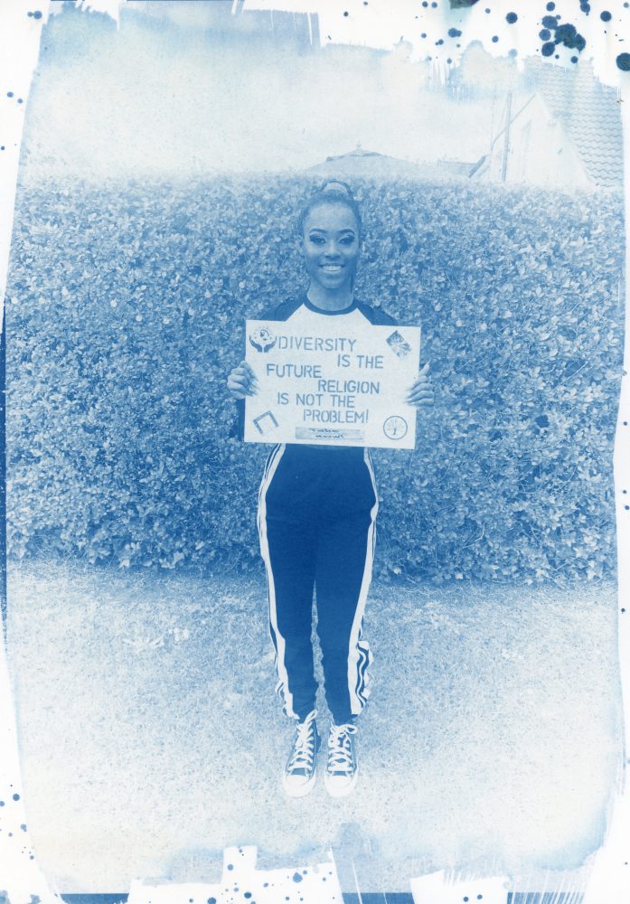 This image shows a young person holding a placard that reads, 