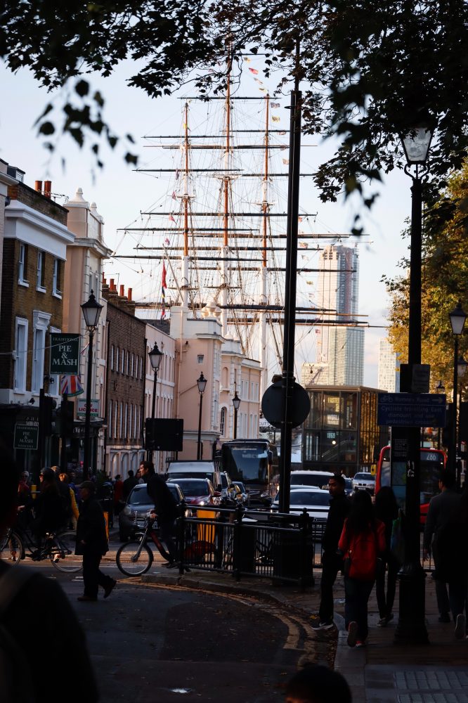 An image of a street in Greenwich with the masts from the Cutty Sark ship appearing above the rooftops.