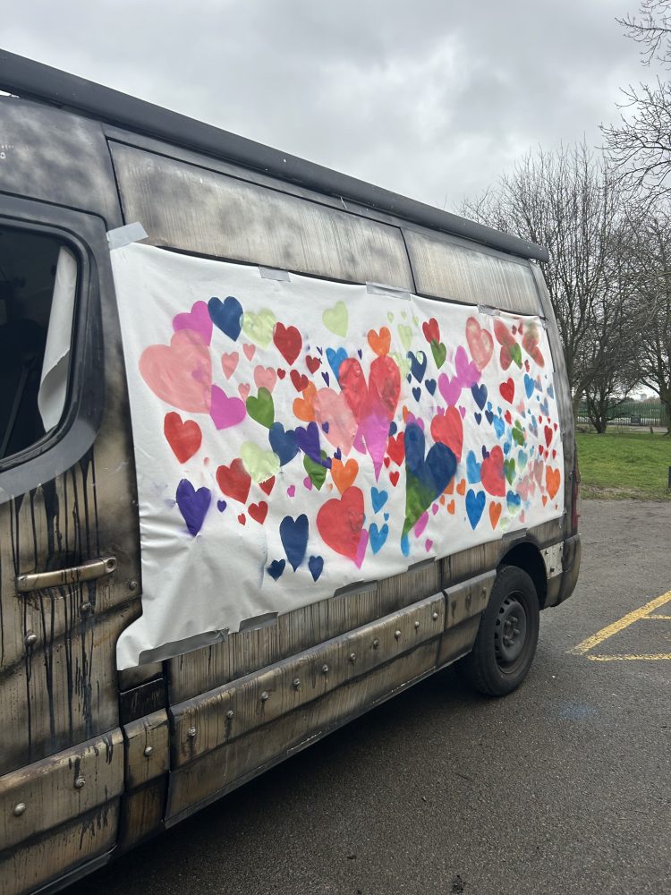 This image shows a banner full of coloured hearts that has been attached to a transit van.