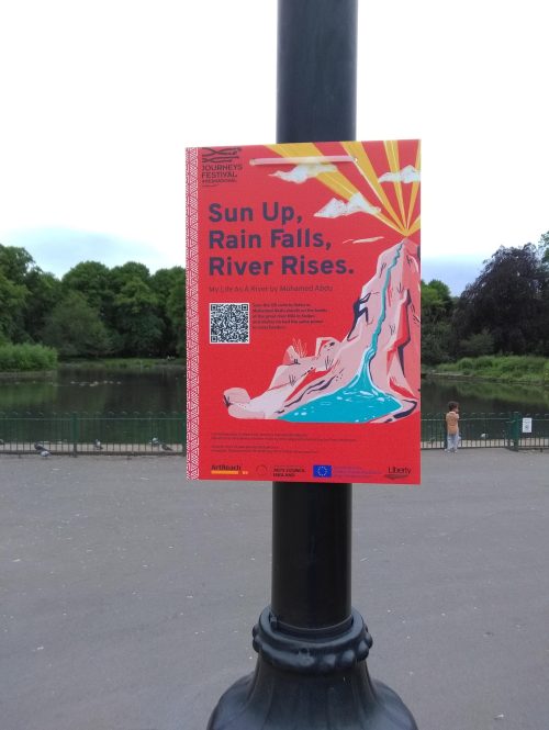 The image shows a red poster with the words Sun Up, Rain Falls, River Rises on it. The poster is tied to a lamppost near a lake and has a QR code to access hidden content.