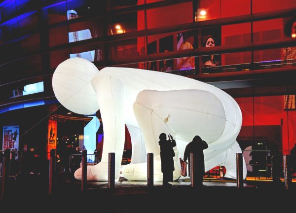 A giant illuminated inflatable crouching down on an outdoor square by night.