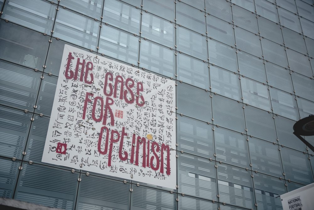 In huge felt letters the words 'The case for optimism' are displayed on a glass wall.