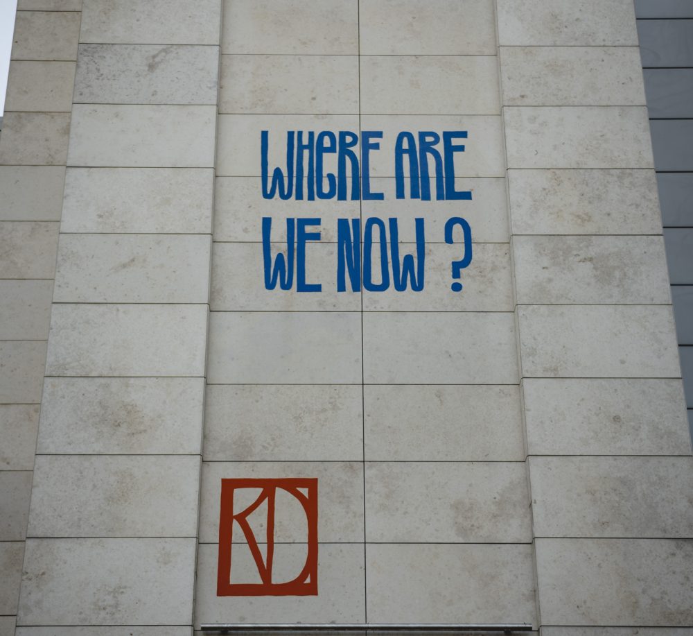 Words, made from felt, that read 'Where are we now?' are displayed on a wall.